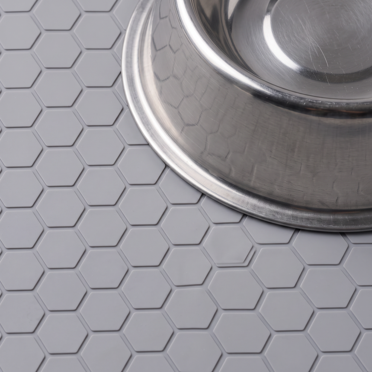 Close-up of a metal bowl resting on the honeycomb-textured gray feeding mat