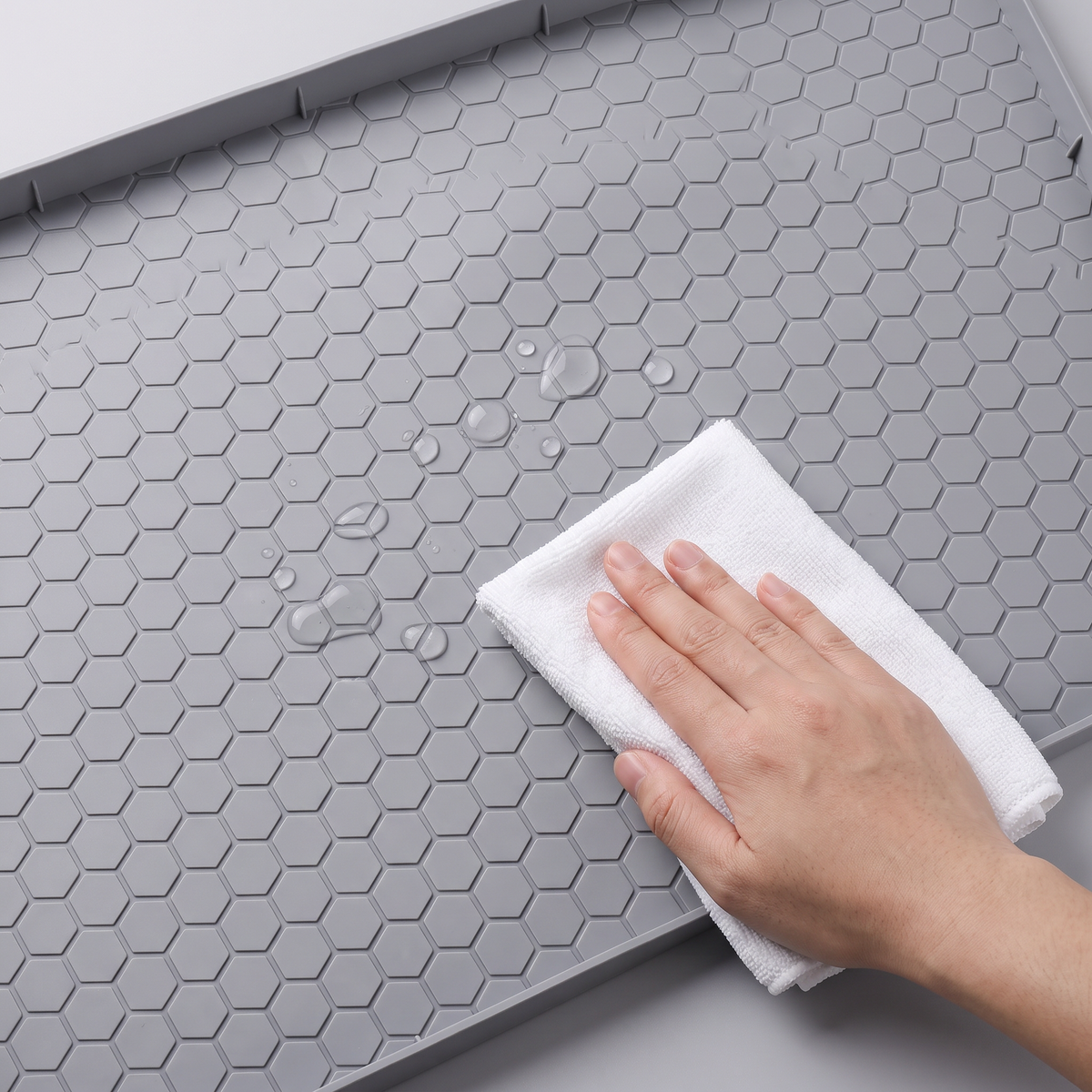 Hand wiping a gray honeycomb-textured feeding mat with a white cloth
