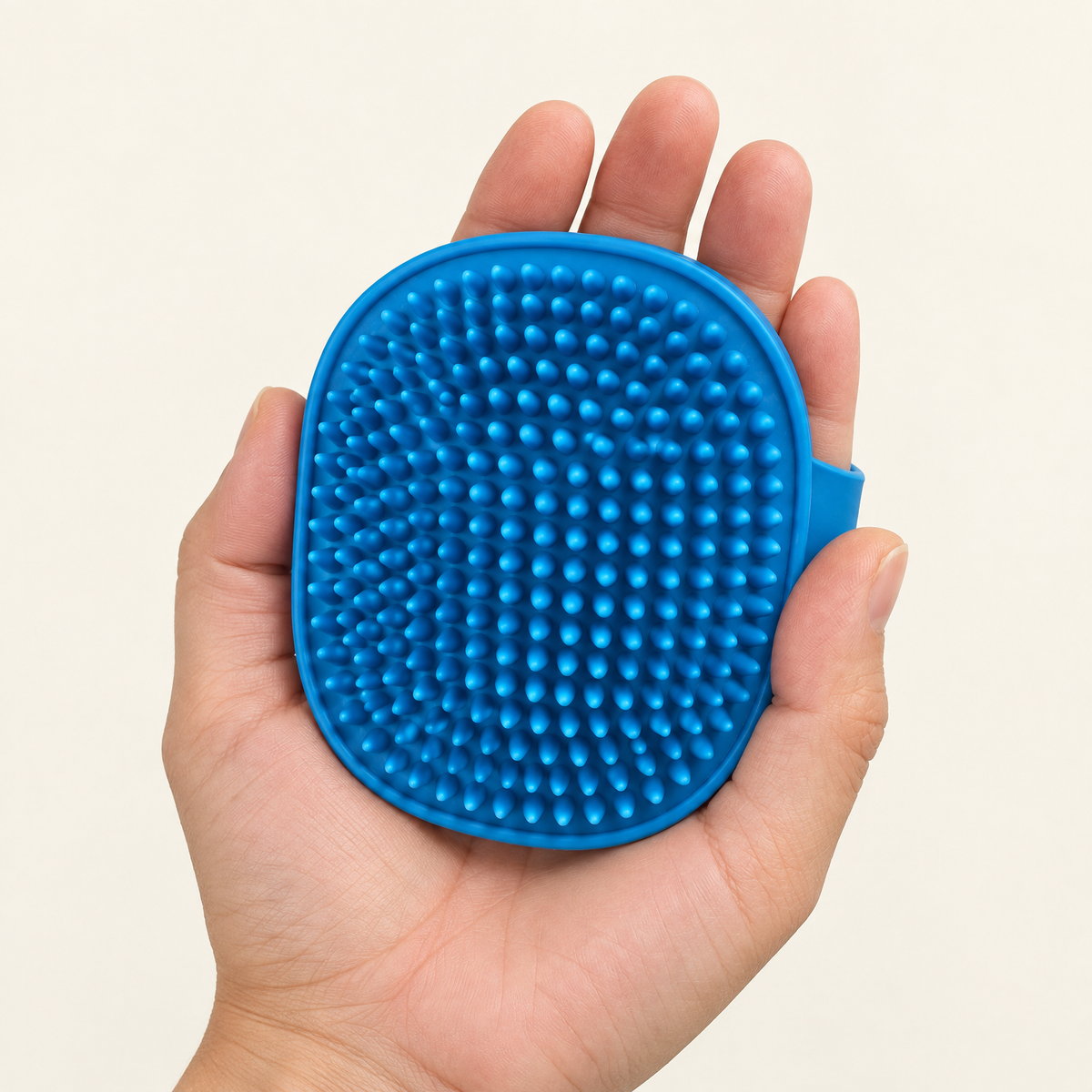 Hand holding the blue silicone cat self-grooming brush with the adjustable strap